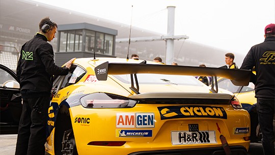Yellow SR Porsche 718 Cayman GT4 with sponsor decals in the pit lane at the Nürburgring